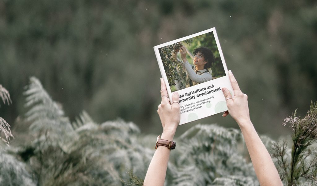 Person holding magazine about urban agriculture and community development, showcasing how books can promote business initiatives