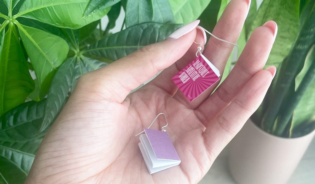 Hand holding two tiny book turned earrings