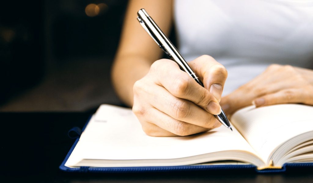 Person writing in a blank journal.