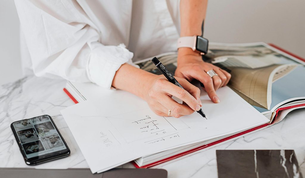 Person making sketches on the inside of a lookbook, showcasing how you can enhance your corporate branding with high-quality printed books