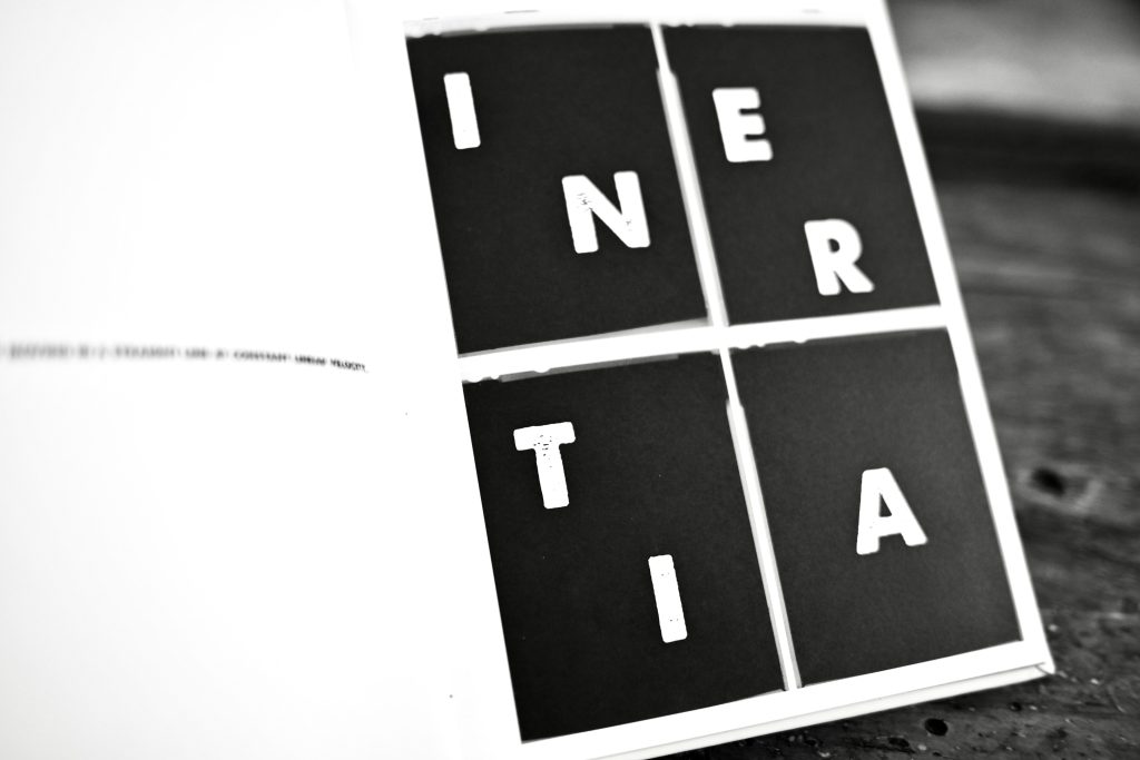 A peek inside a book by Dan Milnor, displaying the title "Inertia," broken across four black squares